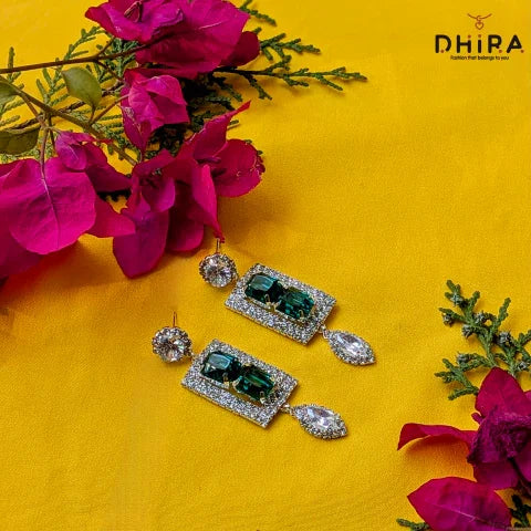Elegant green crystal drop earrings with diamonds on yellow background, surrounded by pink flowers