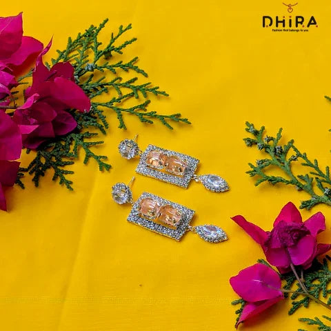 Sparkling rectangular earrings with clear gemstones, displayed on yellow fabric with pink flowers