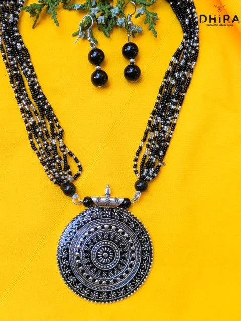 Black beaded necklace with large oxidized silver pendant and matching earrings on yellow background