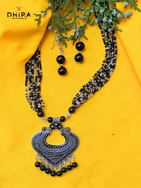 Oxidized silver necklace with black beads and matching earrings on yellow fabric
