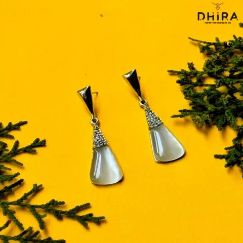 Elegant silver and pearl drop earrings with crystal accents on a yellow background with greenery.