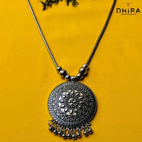 Oxidized silver round pendant necklace with intricate detailing on yellow background